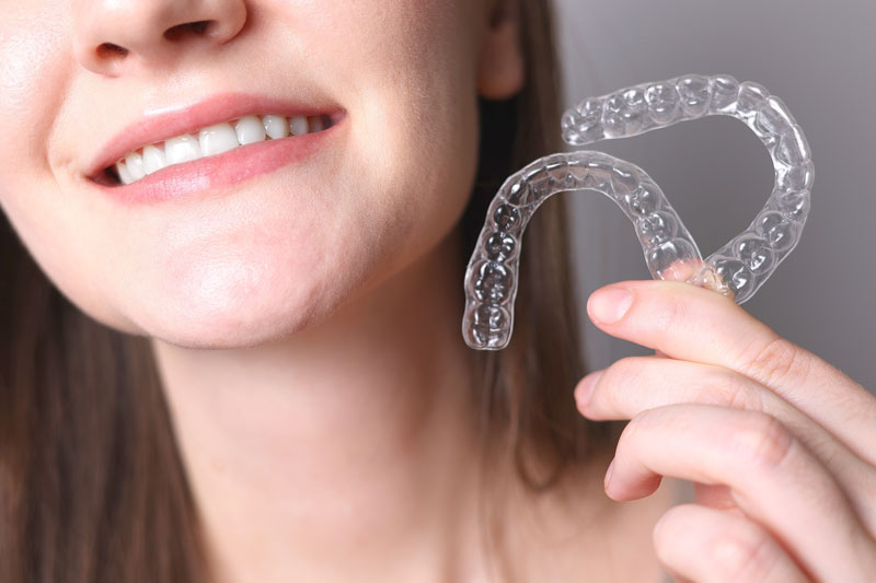a girl smiling holding up 2 invisalign correctors